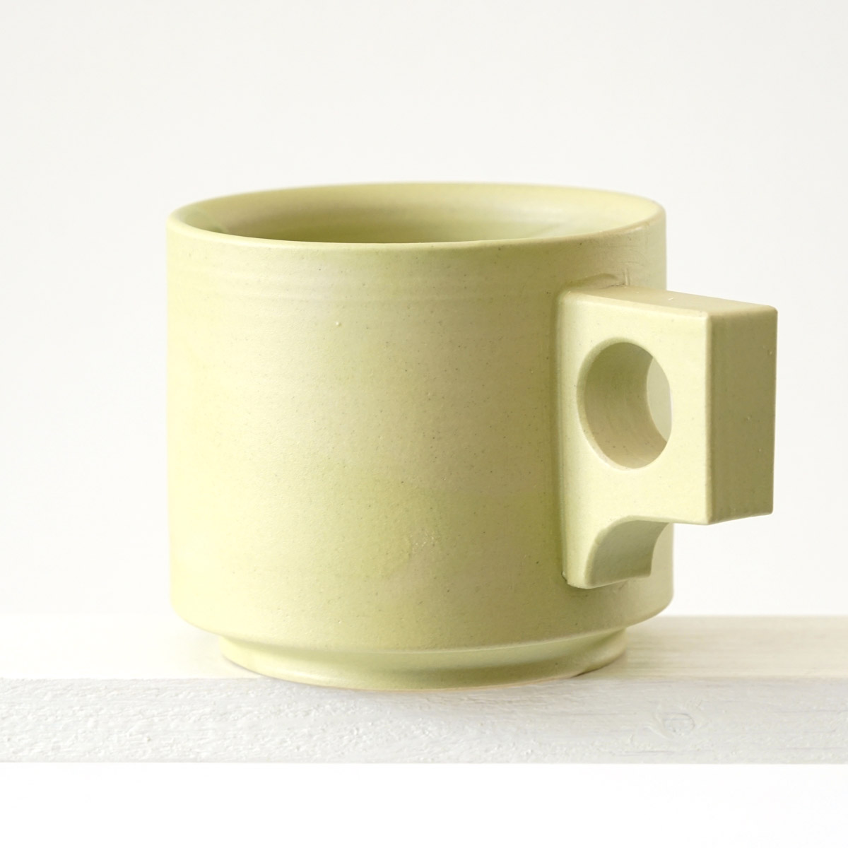 Schräge Ausicht auf eine große Tasse mit einer matten, limonenfarbenen Glasur